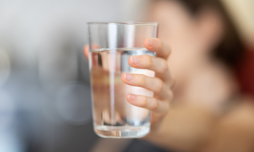 A person is holding a glass of water signifying the importance of water to improve digestion.