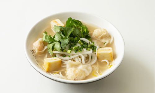 A rice noodle bowl is lying on the table with green leafy vegetables as it is healthier alternative for those who are worried if maggie is healthy or not.