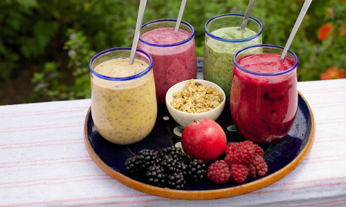 Different types of smoothies with some fruits and nuts are kept in a tray.