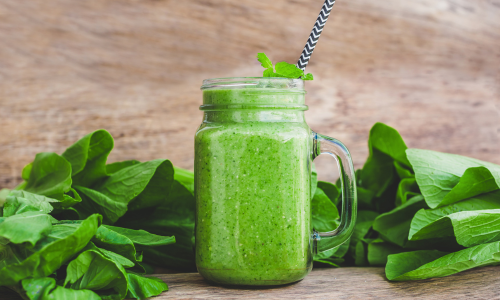 A green smoothie glass made up of spinach is kept with few spinaches.