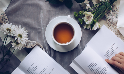 A cup of tea with books and flowers is kept on table.