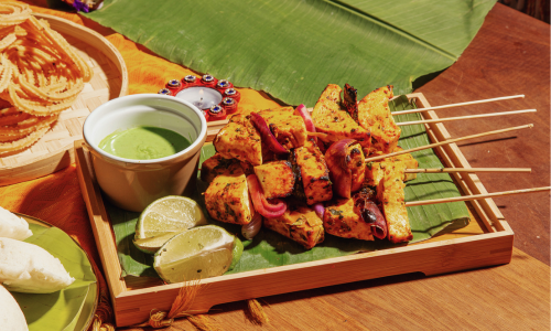 Roasted paneer with green chutney is kept on table.